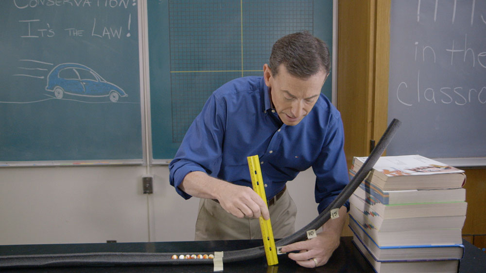 Griff Jones holds a ruler and ramp with marbles.